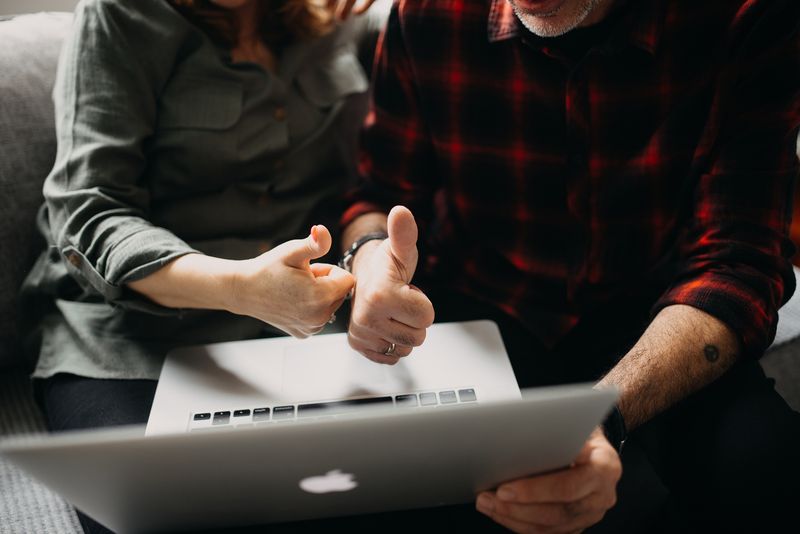 Two people giving a thumbs up while looking at a laptop together