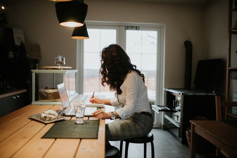 A woman working at a laptop and writing notes in a home office