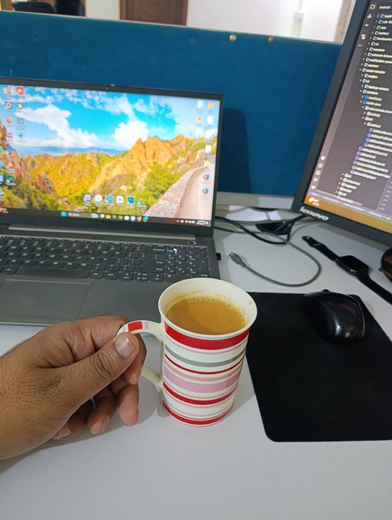 A hand holding a striped mug of tea next to a laptop