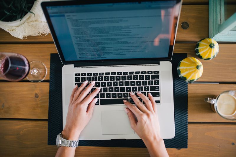 Hands typing on a laptop on a wooden table, seen from above